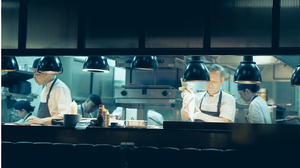 Professional chefs preparing food in a dark kitchen.